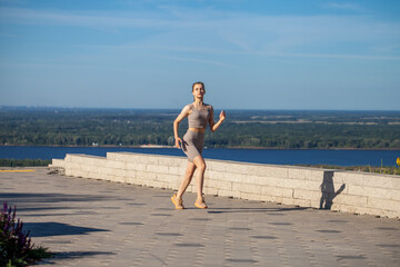 A young woman in a tracksuit performs physical exercises in a summer park
