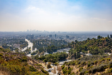 Panoramic view of Los Angeles cityscape with urban skyline and surrounding hills under a clear sky.