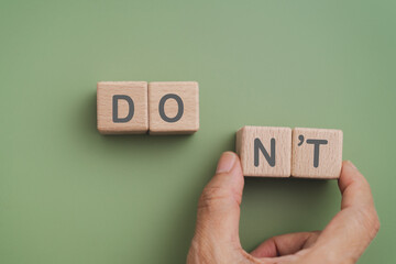 Hand move wooden cube blocks with NT text on green background. For Do's and Don'ts concept