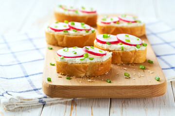 Crunchy baguette slices with cream cheese and herbs on a light kitchen table.