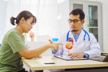 Fototapeta premium A doctor man sits at a desk in a hospital, explaining heart disease symptoms to a female patient. They discuss chest pain, palpitations, fatigue, dizziness, and the risks of myocardial ischemia