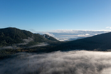 Beautiful aerial drone landscape with clouds over evergreen forests and mountains, captured early morning right after sunrise, in Mount Hood-Lost Lake territory, Oregon