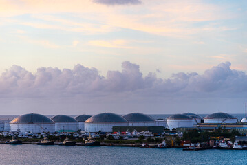 A sunrise view reveals the fuel tanks and structures of a refinery near the port of Freeport, Bahamas. The morning light casts a soft glow over the industrial landscape.