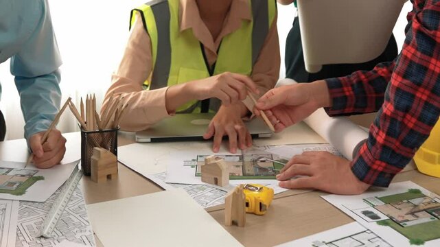 Smart architect and safety engineer discussion about building blueprint on table with architectural document, measurement tools and wooden block scatter around at modern office. Closeup. Delineation.
