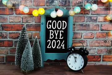 Goodbye 2024 text on blackboard easel stand with alarm clock on wooden and old brick wall background