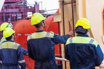 A group of merchant ship crew members stands together during an abandon ship drill, discussing the...