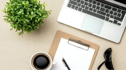 Top view of laptop keyboard, cup of coffee, green domestic plant in small flowerpot, clipboard witn notepaper and pen on beige desk