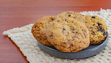 Freshly baked chocolate chip cookies on a dark plate with a rustic woven mat background, ideal for dessert and snack themes.