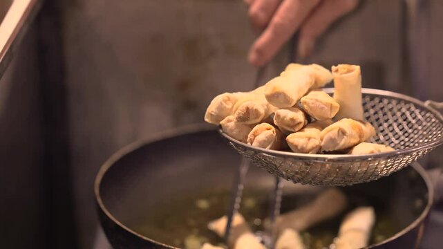 Asian spring rolls frying in oil on a pan at a street food cafe.