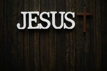 Jesus Christ Text with Wooden Cross Against Dark Wooden Background in Religious Concept