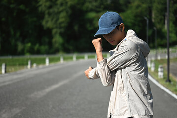 Young sportsman stretching his arms preparing for morning workout in the park