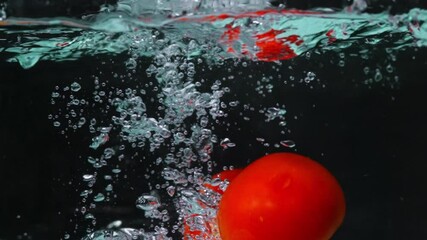 A close up of a fresh vibrant red tomato floating in clear water with black background. Macrography of organic apple falling and dropping in to splashing cool water. Freshness concept. Pabulum. - Powered by Adobe
