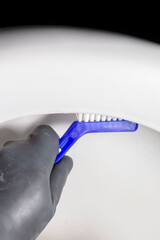 Person, wearing black rubber glove, cleaning toilet lavatory rim with a scrubbing brush. Housework...