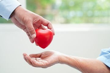 Asian elder senior woman patient holding red heart in hospital.