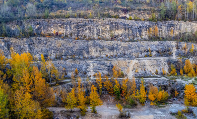 Autumn landscape with ledges of an old limestone quarry, horizontal layers of rocks removed during open-pit mining