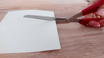 Close up of hand holding scissors and cutting through paper