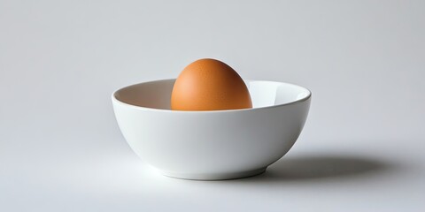 An unadulterated egg nestled in a white bowl, set against a pristine white backdrop. This image features a stark white bowl containing a raw egg, highlighted prominently.