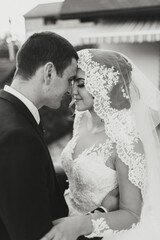 A bride and groom are embracing each other in a wedding photo. The bride is wearing a lace veil and...