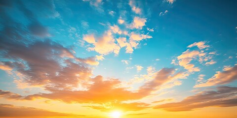 Obraz premium An orange sunrise brightens the soft, fluffy clouds scattered across the clear blue sky, creating a stunning visual display of color and light.