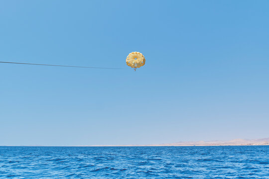 Senior white woman under yellow dome of parachute enjoying parasailing against blue sky, Red Sea