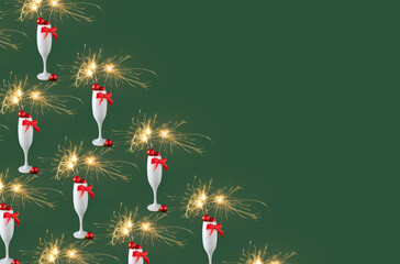 Champagne glass full of christmas decoration, red bow with sparkler on green background. Happy holiday celebration event pattern with copy space.