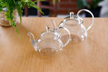 Two empty glass teapots on wooden table with potted plants
