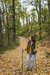 Woman with backpack and trekking poles hiking over the autumn forest