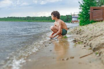 Little smiling healthy curly boy playing with sand on the beach in summer