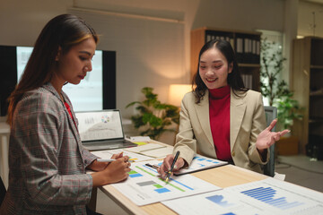 Financial accounting concepts Two businesswomen, confident freelancers working in finance and calculations Discuss management, analysis, and document guidelines on the office board.