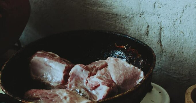 Beautiful close-up shot of an older Latin woman cooking pork prey with oil in a frying pan inside a rustic stone kitchen in a humble village house in Peru.