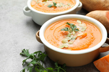 Delicious sweet potato soup with pumpkin seeds in bowls and fresh ingredients on grey table, closeup