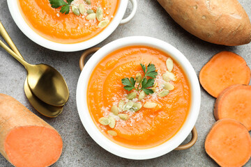 Delicious sweet potato soup with pumpkin seeds in bowls and fresh vegetables on grey textured table, flat lay