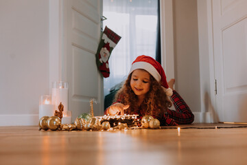A happy little girl is lying on a wooden floor with a Christmas garland