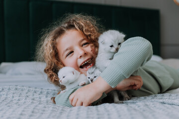 little girl with curly hair hugs little kittens at home