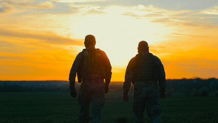 Soldiers Walking in Field During Golden Sunset. Two soldiers in military gear walk across a vast...