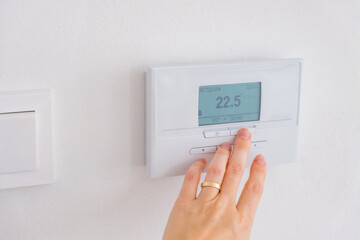 Hand adjusting digital thermostat on wall to control room temperature