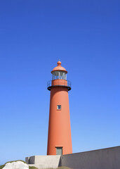 Orange lighthouse in minimalist style against bright blue sky.