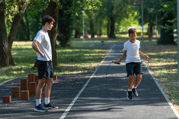 Obraz premium Trainer guides a child in an outdoor jump rope exercise session, focusing on improving coordination, agility, and overall fitness through fun and dynamic physical activity...