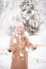 Young happy woman in winter clothes walks in the snowy forest