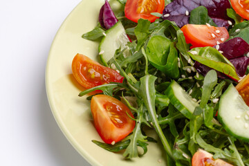 Vegetable salad of tomato, cucumber, greens with sesame on the plate.