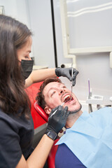 A woman helps a man get his teeth cleaned. The man is smiling, the woman is wearing gloves.