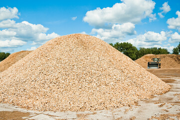 a mountain of wood chips against a background of blue sky and clouds
