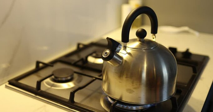 A shiny, polished stainless steel kettle is sitting on a gas stove, fully prepared to brew delicious tea or coffee