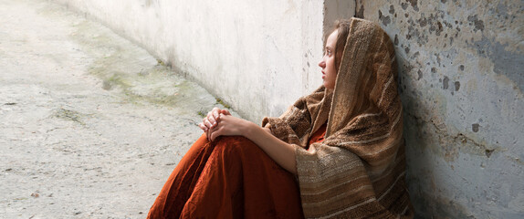 A girl in poor clothes sits on the ground