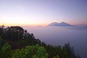 Blur natural nature landscape background of the sunrise view with fog and warm sunlight over mountains. Desa Pinggan, Kintaman, Bali, Indonesia.