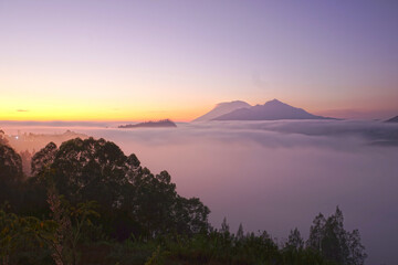 Sunrise view with fog and warm sunlight over the Bali mountains nature landscape of Mount Batur, Mount Abang and Mount Agung from Desa Pinggan, Kintaman, Bali, Indonesia.