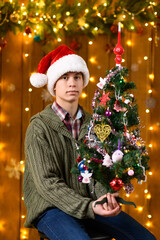 A teenage boy poses in the decorations for the New Year holiday, festive illumination, garland and Christmas tree