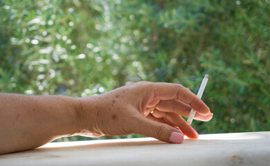 Hand holding a cigarette, surrounded by greenery, depicting smoking outdoors.	