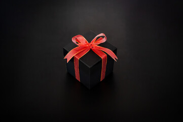 Black gift box with red ribbon tie with the bow puts on black background for Black Friday shopping day concept.