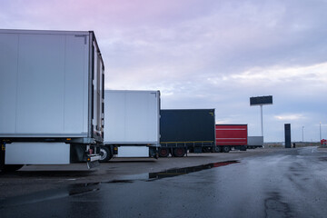 A row of trucks are parked at a service station at dusk to spend the night. The asphalt ground is wet from the rain. Order and symmetry in the transport of goods by road